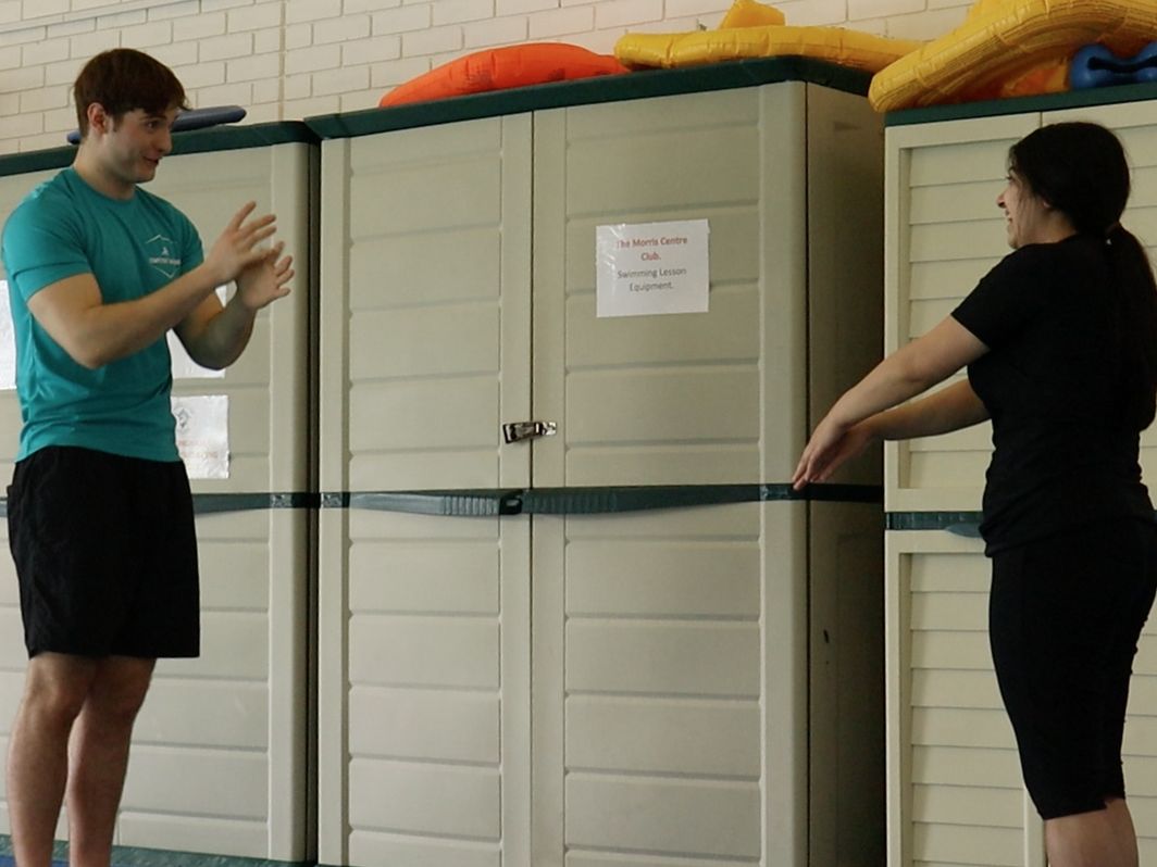 An instructor demonstrating the arm movement to an adult learner on the poolside before they get in