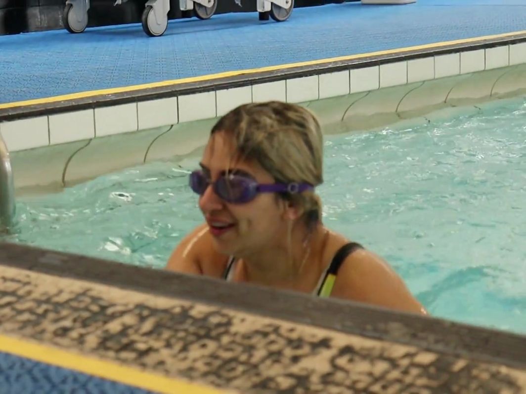 An adult learner at the poolside wall after swimming a length